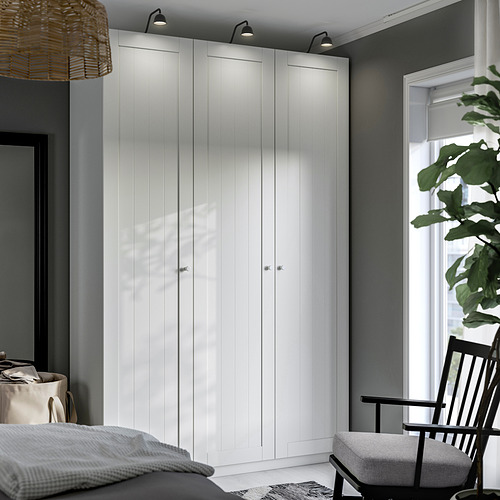 Dormitorio moderno con armario alto blanco PAX, luces, alfombra, silla, cama, cesta de ropa blanca y planta grande.