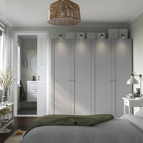 Dormitorio moderno con gran armario PAX gris, mesita de noche blanca, cama con manta verde y puerta abierta al baño.