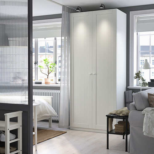 El espacioso armario blanco PAX encaja perfectamente junto a un sofá gris, dominando la habitación con su forma alta y rectangular y su diseño limpio.