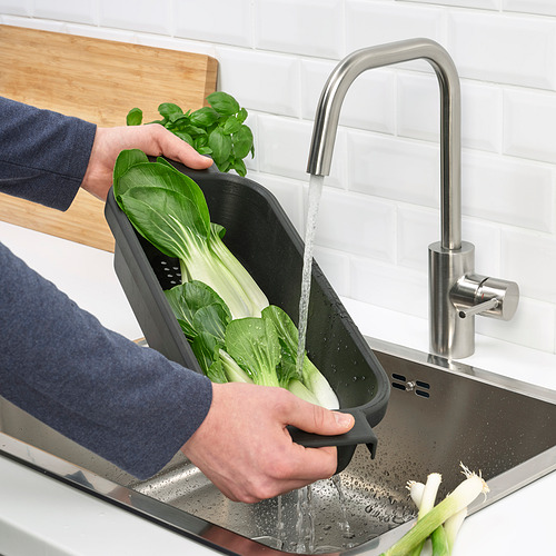 Persona lavando verduras en colador LILLHAVET negro debajo del grifo del fregadero de plata.