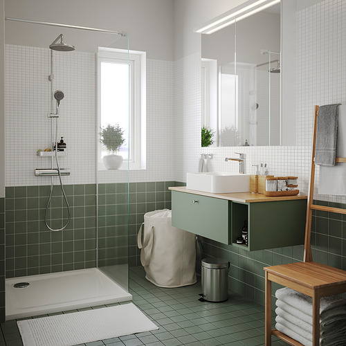 Baño moderno con azulejos verdes, bañera blanca, ducha de vidrio y estante de bambú con combo de silla y toallero.
