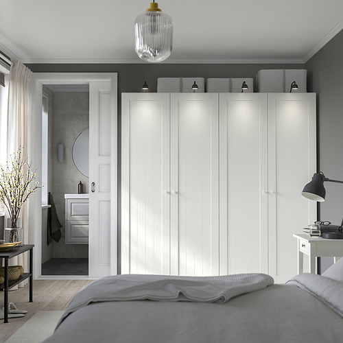 Dormitorio moderno con gran armario blanco, paredes grises, suelo de madera y cama. El armario tiene iluminación integrada. Vista del baño a través de la puerta abierta.