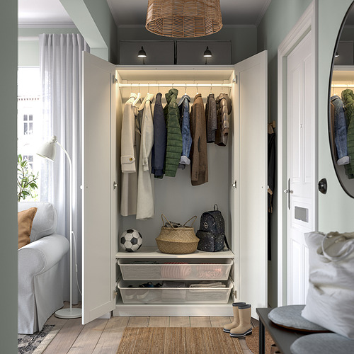 Armario pequeño, blanco, chaquetas y mochila colgadas, puertas abiertas, luz en el interior.
