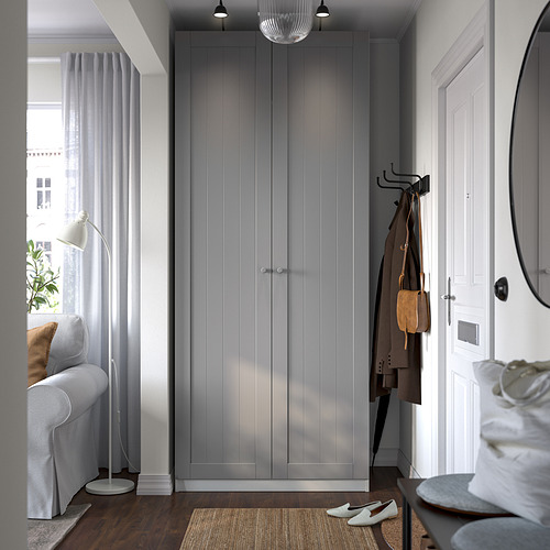 Modern entryway with large grey PAX wardrobe, coat hooks, and a small white armchair by window. Wardrobe is big, tall, and slender.