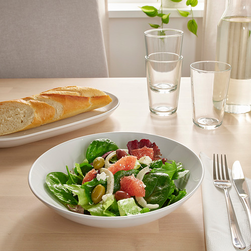 Una mesa de madera con un plato de ensalada verde, una baguette en rodajas y vasos.