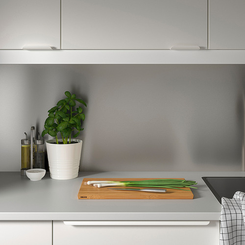 Encimera de cocina gris minimalista. Pequeña planta en maceta, botellas de aceite, cuchillo, cebolletas y tabla de cortar con panel de pared LYSEKIL.