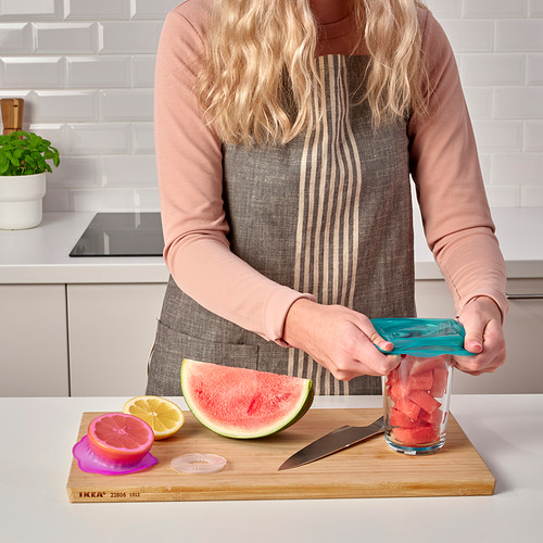 Una persona usa cubiertas de silicona para alimentos para sellar un frasco de vidrio con trozos de sandía. Destaca la función de los productos de mantener los alimentos frescos.
