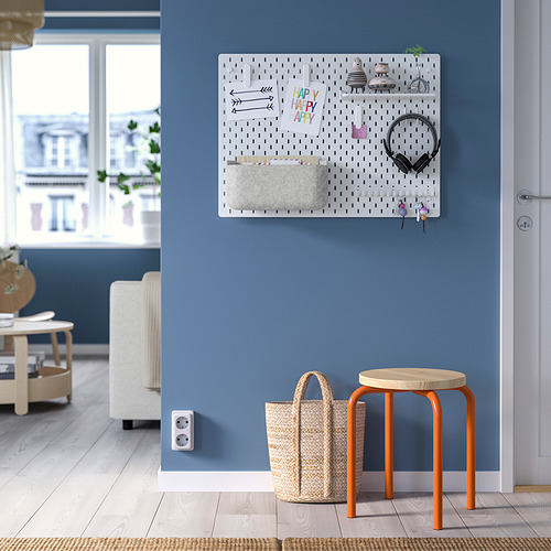Pared azul con tablero perforado SKÅDIS blanco y taburete naranja que sostiene una cesta blanca.