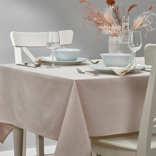 Mesa con sillas y cuencos blancos, vasos y jarrón decorativo sobre un mantel de rayas beige.