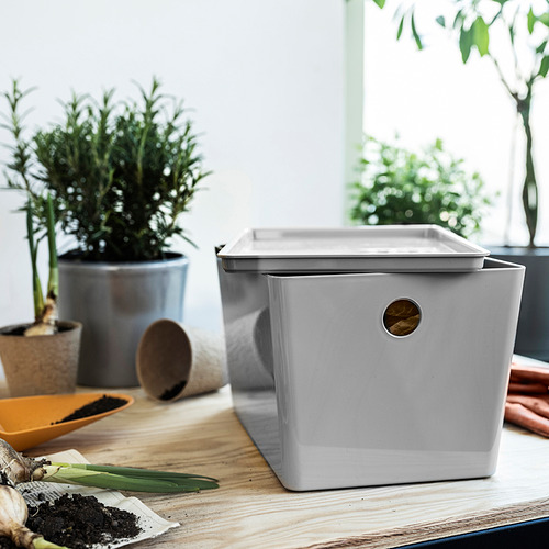 Caja KUGGIS gris con asa, rodeada de plantas y herramientas. De tamaño mediano, fabricado a partir de plástico reciclado.