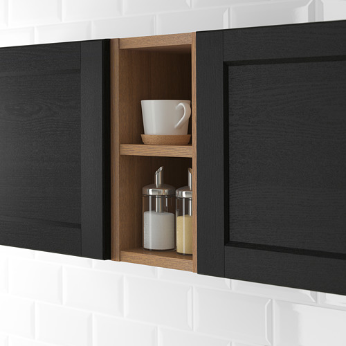 Mueble de cocina negro con sección abierta, con una taza blanca, un tazón pequeño y dos frascos de especias en estantes de madera clara.
