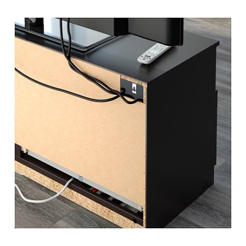 Mueble de tv negro con gestión de cables y mando a distancia en la parte superior.