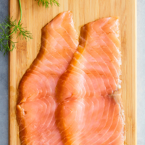 Filetes de salmón rosado sobre tabla de madera con hierbas verdes.