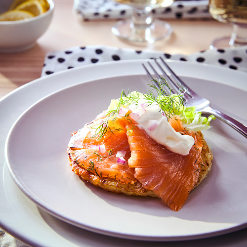 Un plato de salmón ahumado en frío sobre una rebanada de pan tostado, adornado con crema, eneldo y cebollas rojas en un plato morado.