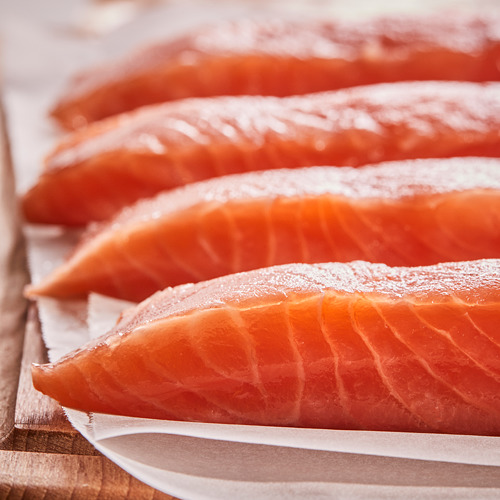 Filetes de salmón fresco colocados sobre papel pergamino, que muestran una textura firme y húmeda y un color rico y natural. Exhibido sobre una superficie de madera.