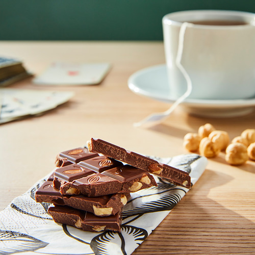 Barras de chocolate apiladas, algunas con nueces, en una servilleta estampada cerca de una taza de café.