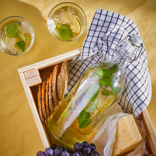 Caja de madera con jarra de bebida de flor de saúco, queso, uvas, vasos y tela.