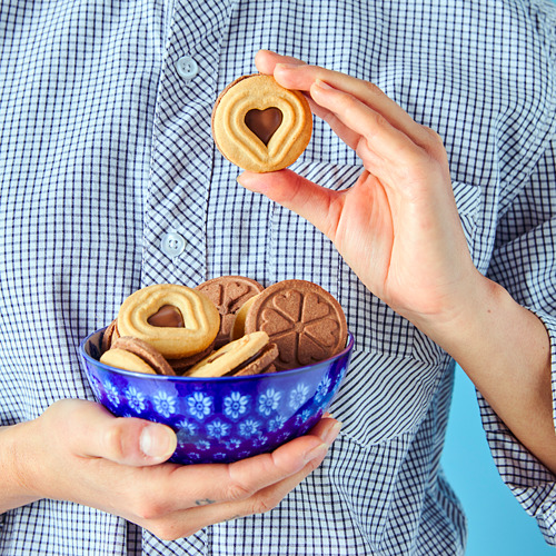 Persona sosteniendo un tazón azul lleno de galletas en forma de corazón y una sola galleta en forma de corazón a la que le falta un bocado.