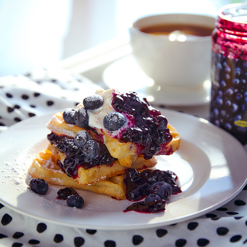Gofres de arándanos con nata y café en un plato blanco. Desayuno, luminoso, acogedor y delicioso.