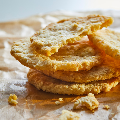 Pila de galletas de avena doradas, redondas y crujientes sobre un paño marrón.