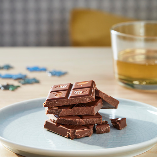 Plato de barras de chocolate marrón apiladas, vaso de líquido al lado, piezas de juego azules cerca.