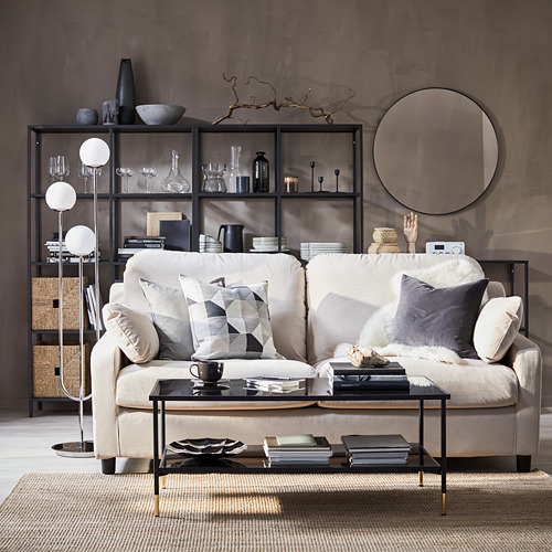 Sala de estar moderna con sofá crema, mesa de centro negra, lámpara elegante, libros y artículos decorativos.