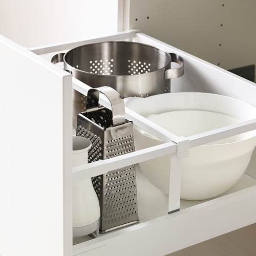 Gabinete de cocina blanco abierto que exhibe ralladores de queso, colador y tazones para mezclar en un estante ajustable.