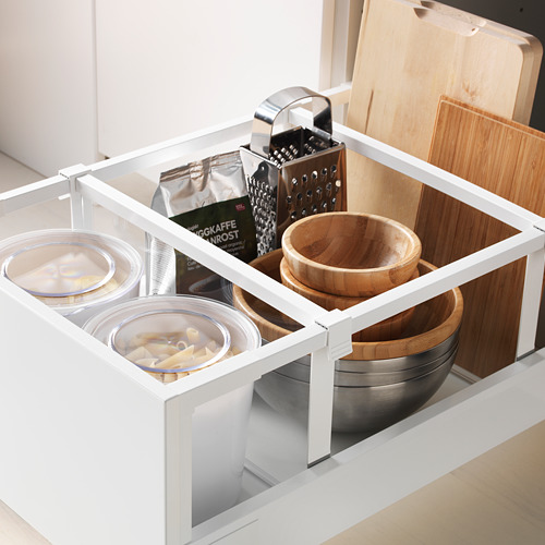 Cajón de cocina organizado con tazones de vidrio, utensilios de madera y rallador de metal en gabinete blanco.
