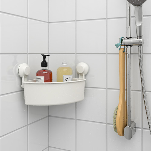 Un rincón de baño con un estante de ventosa que contiene botellas de champú y jabón. Un cepillo de madera cuelga junto a una ducha en la pared de azulejos.