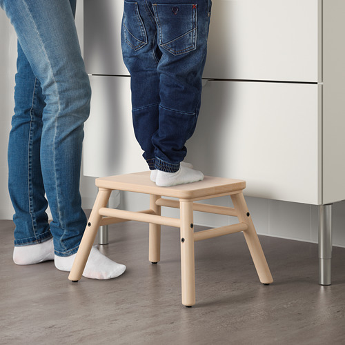 Dos personas utilizan un taburete de madera, una de pie sobre él, probablemente para llegar a zonas más altas, mostrando su función como taburete.