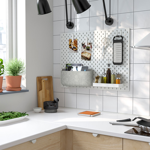Cocina moderna con tablero perforado SKÅDIS que sostiene cestas grises, botellas y utensilios.