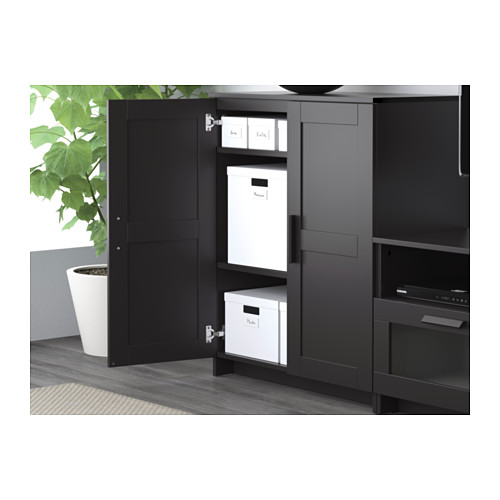 Mueble de televisión negro con puertas abiertas que dejan ver estantes y cajas de almacenamiento blancas, colocadas contra una pared gris.