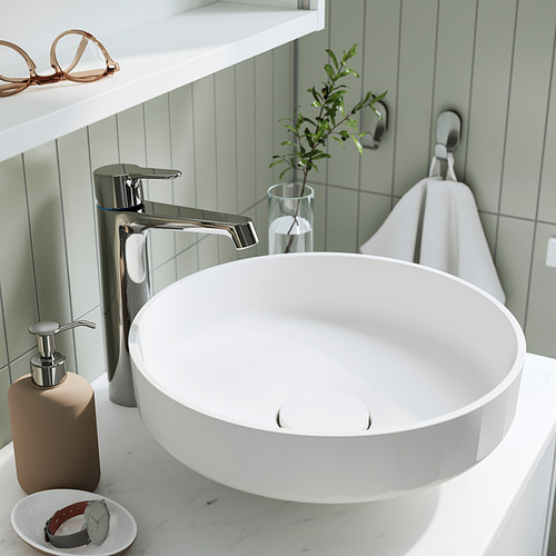 Un lavabo de baño moderno con grifo monomando cromado. Realizada en mármol triturado, se asienta sobre una encimera blanca, con un lavabo circular y un diseño sencillo.