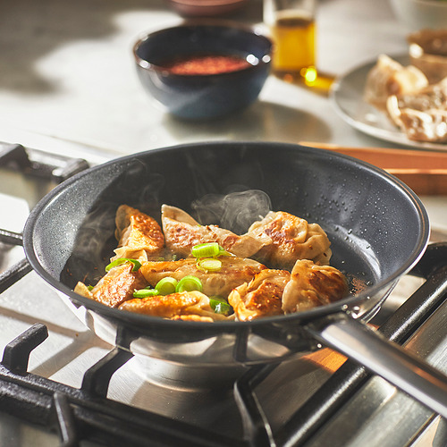 Sartén en una estufa cocinando albóndigas. El vapor sube, mostrando su calor. Las cebollas verdes adornan la comida.