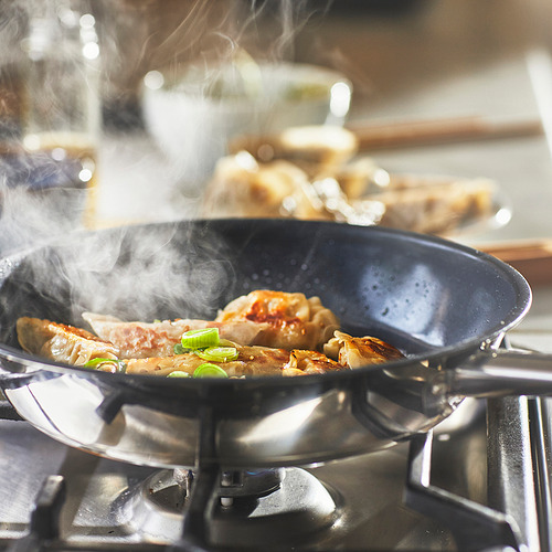 Descripción de la imagen: una sartén negra en una estufa, cocinando albóndigas y verduras. El vapor sube, lo que indica una cocción activa.