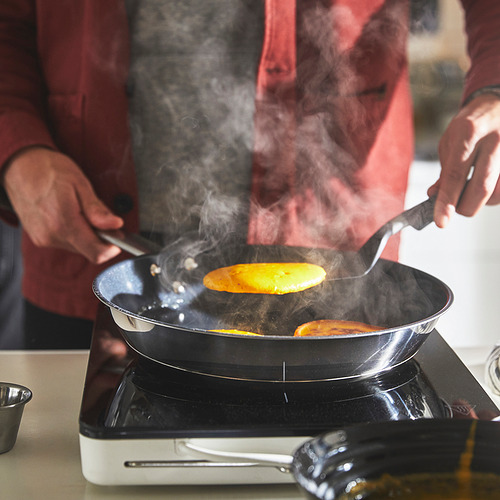 Persona cocinando en una sartén con vapor subiendo, probablemente usando una sartén antiadherente IKEA 365+ en una estufa eléctrica.