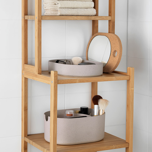 Estantería de baño de madera con un cuenco con brochas de maquillaje y otro con objetos pequeños, y un espejo redondo con marco de corcho en la estantería superior.