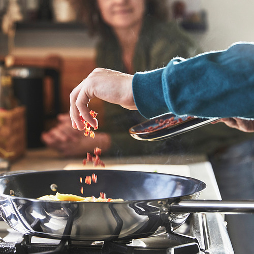 Cocinar con sartén en la estufa, agregando alimentos.