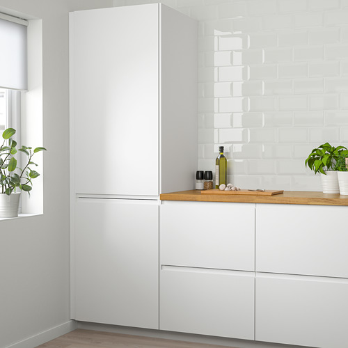 Moderna cocina blanca con armarios VOXTORP, electrodomésticos y nevera empotrada. Mostrador de madera con plantas y utensilios de cocina.