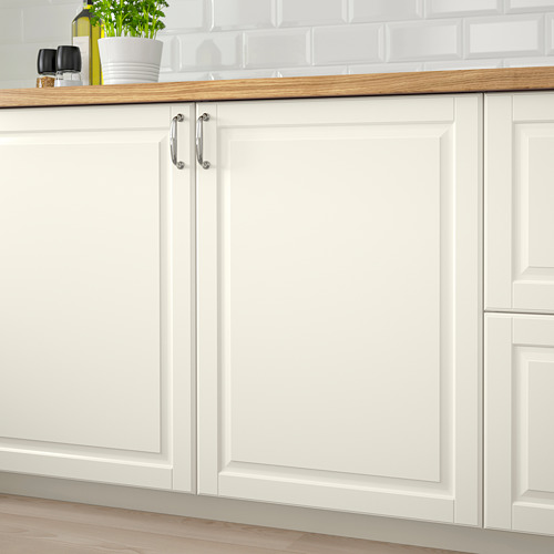 Gabinetes de cocina blancos con paneles biselados de color blanquecino, encimera de madera, manijas plateadas y placa para salpicaduras de azulejos blancos en una configuración limpia y moderna.