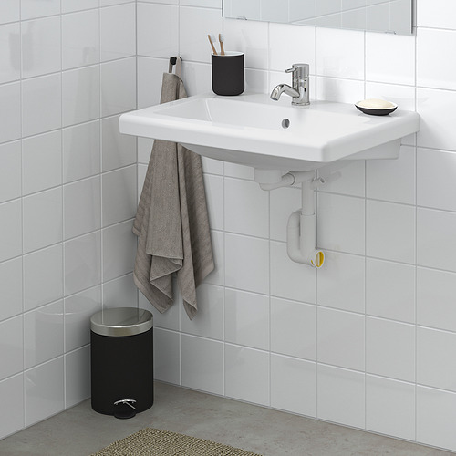 Baño moderno con lavabo blanco TVÄLLEN, grifo plateado, toalla gris, papelera negra, pared de azulejos limpios.
