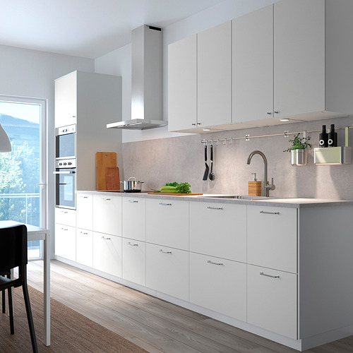 Cocina moderna con gabinetes blancos, electrodomésticos de acero inoxidable, tablas de cortar de madera y herramientas para colgar.