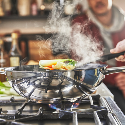 En un wok de acero inoxidable con revestimiento antiadherente se cocinan alimentos coloridos en una estufa de gas, emitiendo vapor.