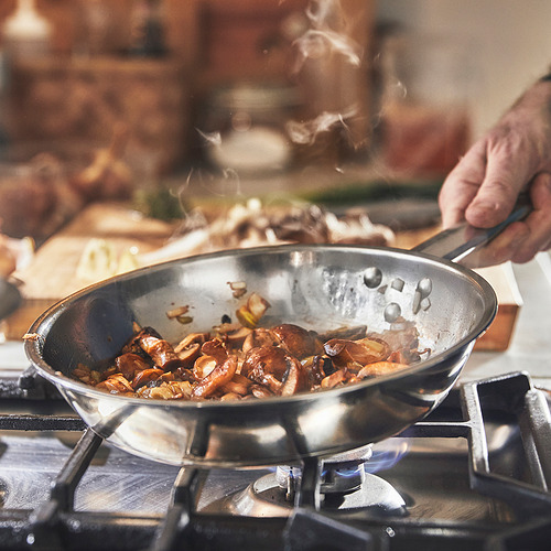 Cocinar champiñones en una sartén de acero inoxidable en una estufa de gas.