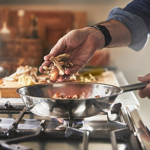 Una persona está cocinando agregando champiñones a una sartén chisporroteante en una estufa de gas.