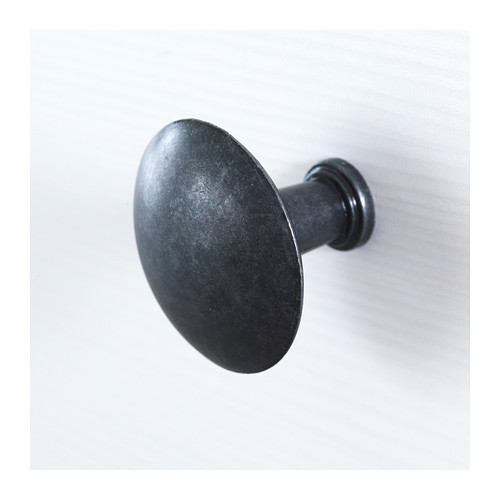 Gancho de pared de metal negro con un diseño liso y ligeramente redondeado, montado de forma segura sobre una pared blanca.