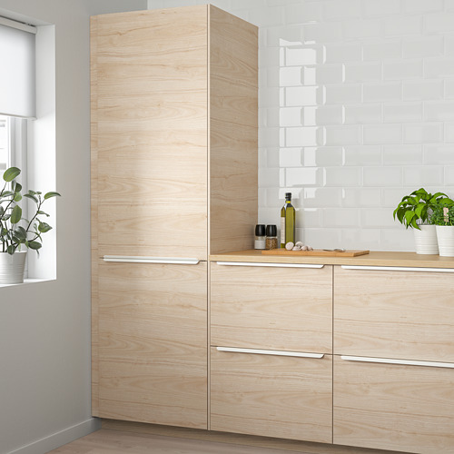 Cocina moderna con gabinetes de madera de color beige claro, placa para salpicaduras blanca y plantas en macetas. Los gabinetes tienen un diseño elegante y alto.