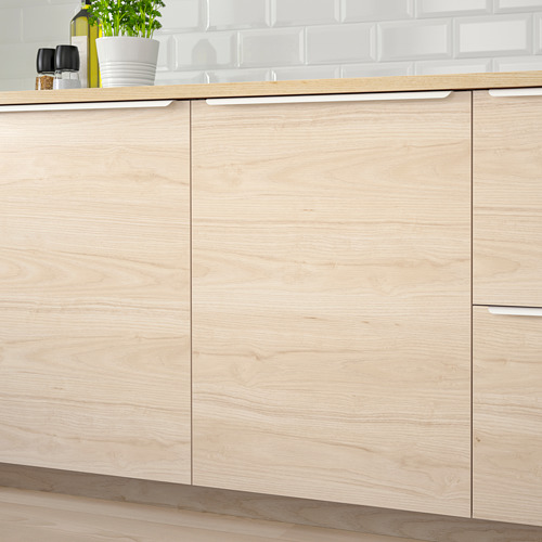 Muebles de cocina de madera con acabado en fresno, superficies de fácil limpieza, diseño moderno, tirador integrado, azulejos blancos, encimera de madera con botella y planta.