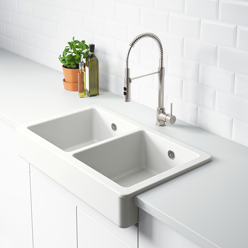 Un fregadero de cocina moderno con un lavabo doble blanco y un grifo elegante, con una planta verde y dos botellas de vidrio al lado.