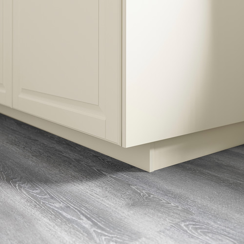 Base de mueble de cocina blanca con zócalo adjunto, que descansa sobre un suelo gris con motivos de madera.